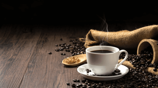 Hot coffee in a white coffee cup and many coffee beans placed around and sugar on a wooden table in a warm light atmosphere, on dark background, with copy space