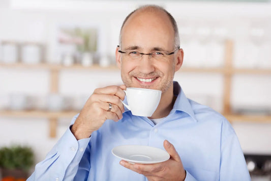 older man in blue shirt and glasses holding a small coffee cup and plate